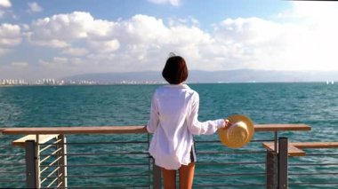 Hasır şapka takan ve okyanusa bakan bir kadın. Deniz kenarında yaz tatili. Deniz kenarında sakin ve sakin bir hayat. Özgürlük ve