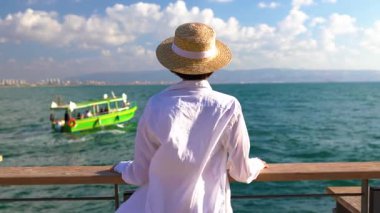 Bir kız denizin kenarında duruyor ve geçen bir gemiye bakıyor. Bir kız seyahat eder ve tatilinin tadını çıkarır. Huzur ve rahatlama.