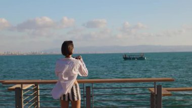 Kameralı kız. Güzel bir turist tatil boyunca deniz manzarasının tadını çıkarıyor ve geminin fotoğraflarını çekiyor. Şık kız.