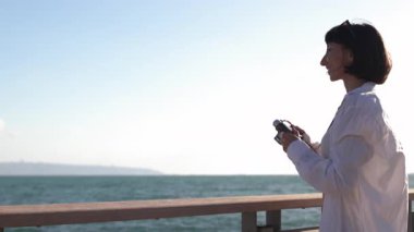 Kameralı kız. Güzel bir turist tatil boyunca deniz manzarasının tadını çıkarıyor ve kamerasıyla fotoğraf çekiyor. şık kız.
