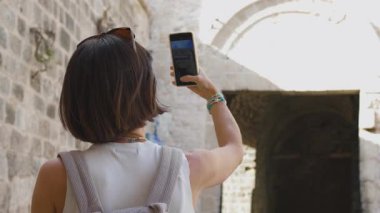 Gülümseyen neşeli bir kadın Arap ülkesinde eski bir şehrin caddesinde yürüyor. Şık gezgin şehir simgelerinin resimlerini çekiyor.