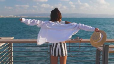 Hasır şapkalı ince kadın denize bakıyor ve anın tadını çıkarıyor. Özgürlük ve neşe. Deniz kenarında yaz tatili. Plaj yaşam tarzı.