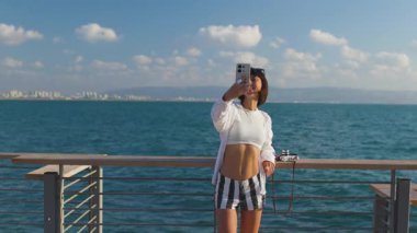 Dişi gezgin, manzaralı tahta yolda altın günbatımı selfie 'sini çekiyor. Avrupa seyahati. Yaşam tarzı, tatil, turizm, doğa, aktif