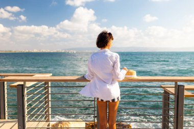 Elinde hasır şapkası olan ince bir kadın okyanusa bakıyor. Deniz kenarında yaz tatili. Plaj hayatı. Deniz kıyısında özgürlük ve rahatlama.