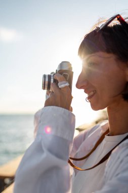 Kameralı kız. Güzel bir turist tatil boyunca deniz manzarasının tadını çıkarıyor ve kamerasıyla fotoğraf çekiyor. Tatildeki şık kız..