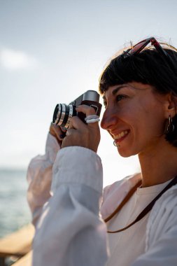 Kameralı kız. Güzel bir turist tatil boyunca deniz manzarasının tadını çıkarıyor ve kamerasıyla fotoğraf çekiyor. Tatildeki şık kız..