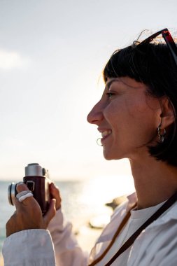 Kameralı kız. Güzel bir turist tatil boyunca deniz manzarasının tadını çıkarıyor ve kamerasıyla fotoğraf çekiyor. Tatildeki şık kız..