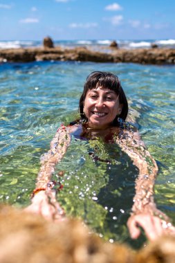 Kırmızı mayo giyen ince kız güneşli bir günde denizde yüzmekten hoşlanır. Yaz havası. Kız yüzüyor ve rahatlıyor. Mayolu genç esmer..