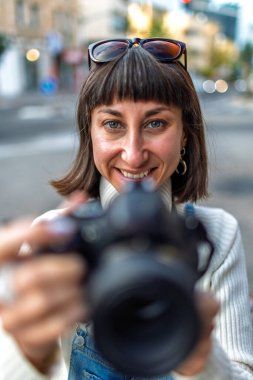 Şık giyinmiş, şehrin fotoğraflarını çeken güzel, neşeli fotoğrafçı kız. Dışarıda fotoğraf çeken genç bir kız. Sokak fotoğrafı..