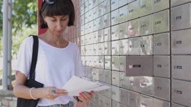 Posta kutusunun yanında duran zarflara bakan genç bir kadın. Posta alıcısı. Sokakta duran zarif kızın yakın plan portresi.