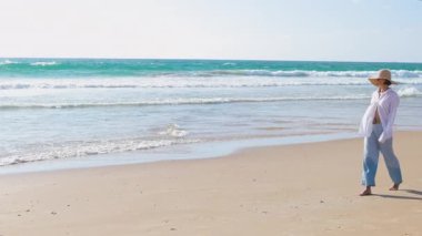 Genç ve ince esmer kumsalda tek başına yürüyor. Kumda deniz kenarında ya da okyanusta günlük kıyafetlerle yürüyen bir kız. Plaj tatili