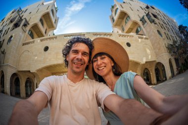 Yaz kıyafetleri içinde genç bir çift şehir caddesinde yürürken birbirlerine sarılıp selfie çekiyorlar. Sokakta selfie.