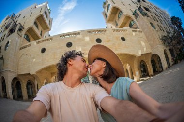 Yaz kıyafetleri içinde aşık genç bir çift şehir caddesinde yürürken öpüşüp selfie çekiyorlar. Sokakta öpücük.