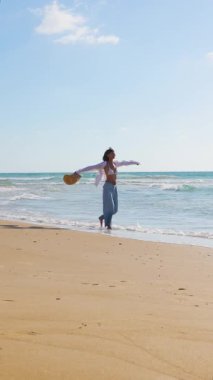Dikey çekim. Genç ve ince esmer kumsalda tek başına yürüyor. Kumda deniz kenarında ya da okyanusta günlük kıyafetlerle yürüyen bir kız. Plaj