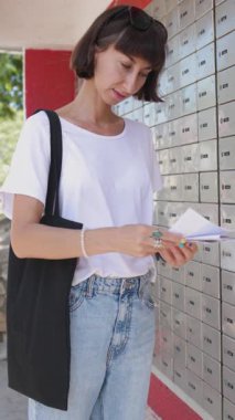 Dikey çekim. Posta kutusunun yanında duran zarflara bakan genç bir kadın. Posta alıcısı. Ayakta duran zarif kızın yakın plan portresi.