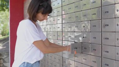 Mektubu okuyan kadın posta kutularının arasında duruyor. Posta kutusunu açan gülümseyen genç bir kadının portresi.