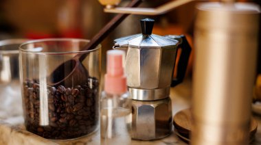 Evdeki masada Moka pot var. Kahve yapma konsepti. Moka demliği, fasulye spreyi, kahve öğütücü, mutfak masasının üzerinde duran bir kavanoz kahve çekirdeği. Kahve yapmak için gerekli malzemeler.
