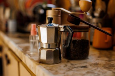 Kahve yapmak için gerekli malzemeler. Moka demliği, fasulye spreyi, kahve değirmeni ve kahve çekirdekleri mutfak masasında duruyor. Kahve yapma konsepti.