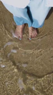 Dikey çekim. Bir kız kumda çıplak ayakla yürümekten ve berrak tropikal okyanustan hoşlanır. Pov çekimi, yakın çekim. Yalınayak yürümenin zevki