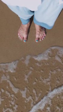 Dikey çekim. Bir kız sahilde yürüyor. POV, deniz kumu üzerinde duran bir kadının ayaklarının yakın çekimi. Yürümenin zevki