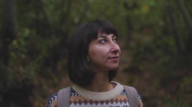 Sırt çantalı bir kız etrafına bakıyor, çevresindeki doğanın ve romantik havanın tadını çıkarıyor. Yüzüne yakın çekim. Bir kız...