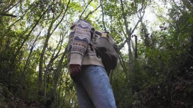 Bir kız sırtında bir sırt çantasıyla orman yolunda duruyor. Etrafına bakınıyor, çevresindeki doğanın tadını çıkarıyor.