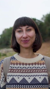 Dikey çekim. Sırt çantalı bir kız kameraya bakar ve gülümser. Doğanın tadını çıkaran ve romantik bir ruh hali içinde bir kadın. Ona yakın çekim.