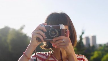 Şık bir esmer, fotoğraf çekmek üzere olan bir kamerayı yüzüne tutuyordu. Parlak bir gökyüzü altında hareketi yakalıyor.