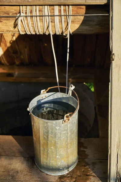 Metal bucket full of fresh water just taken up from a old wooden draw-well at countryside in a hot summer day