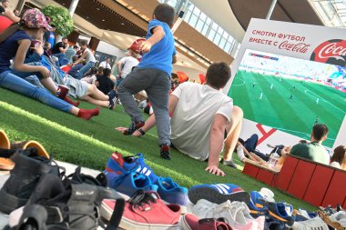 Moskova, Rusya - Haziran 16,2018. FIFA Dünya Kupası yayın büyük alışveriş merkezinde bir yapay çim üzerinde sol onların ayakkabı dışında oturan Mega büyük ekranda izlerken insan kalabalığı