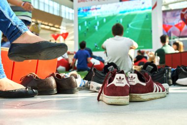 Moskova, Rusya - Haziran 16,2018. FIFA Dünya Kupası yayın büyük alışveriş merkezinde bir yapay çim üzerinde sol onların ayakkabı dışında oturan Mega büyük ekranda izlerken insan kalabalığı