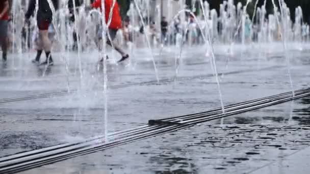 Lanzamiento en cámara lenta de pulverizaciones de agua de una fuente de suelo y jóvenes corriendo y saltando a través de ella disfrutando de la vida — Vídeos de Stock