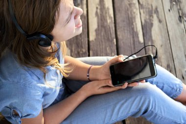 Müzik kulaklık ve bir akıllı telefon ile açık havada yaz akşamları keyfi kapalı gözlü genç kız. Yukarıdan görüntülemek.