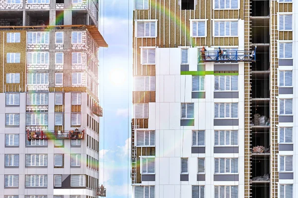 Munkavállalók a falakon, a nap süt, az épületek között építés alatt két lakossági épületek építési bölcsők — Stock Fotó