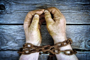 Eski paslı kalın zincirli bir kopya alanı ile ahşap kurullarında zincirli kirli eller erkek. Unfreedom kavramı.