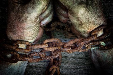 Powerful dirty male hands clenched into fists chained with rusty chain on wooden background clipart