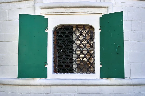 Church window with green metal shutters in russian medieval monastery