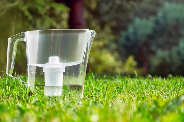 Water filter jug standing on the green grass in summer garden