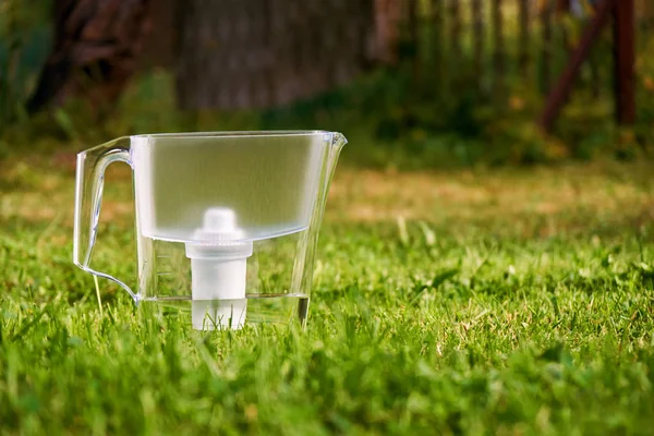 Кувшин водяного фильтра стоит на зеленой траве в летнем саду — стоковое фото