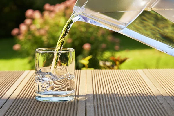 Dökülen açık su filtrasyon sürahi su bir bardak yeşil yaz bahçe arka planda bir sıcak içine güneşli yaz günü filtre