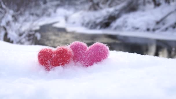 Красные и розовые шерстяные сердца на белом снегу на берегу реки зимой — стоковое видео