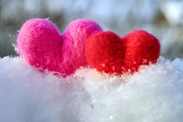 Two wool red and pink hearts standing on the white fluffy snow in winter. Symbols of love. Love, healtcare, valentines day concept.