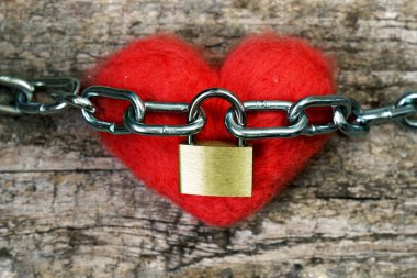 Kırmızı oyuncak kalp bir zincirle sarılmış ve metal bir kilit ile kapalı. Aşk kavramı.