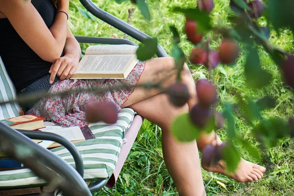 Tiener meisje leest een boek, zittend op een tuin schommel in de zomertuin. — Stockfoto