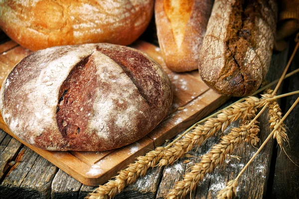 Baked bread of different types and shapes and wheat ears on the wooden boards — Stock Photo, Image