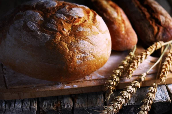 Freshly baked bread and wheat ears on the old wooden table in the dark — Stock Photo, Image