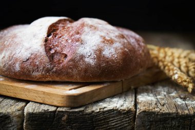Eski ahşap masada yuvarlak ekmek ve buğday kulakları