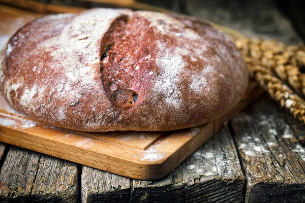 Round bread and wheat ears on the old wooden table — Stock Photo, Image