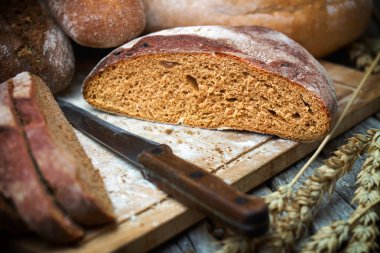 Eski ahşap masada bir bıçak ile dilimlenmiş çavdar yuvarlak ekmek ve buğday kulakları