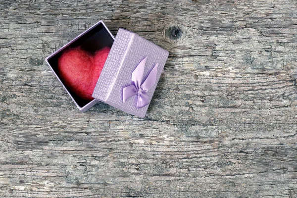 Red wool toy heart lying in a open gift box on a wooden table. Heart as a gift.